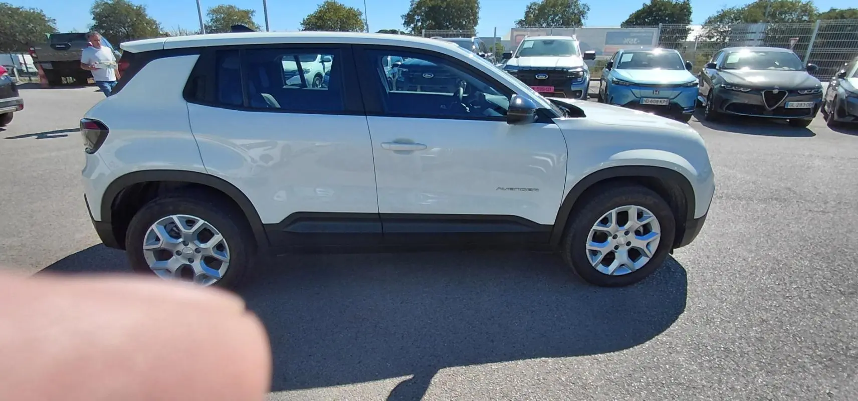 Jeep Avenger blanc vu de profil côté gauche, avec jantes alliage et protections noires sur les bas de caisse.