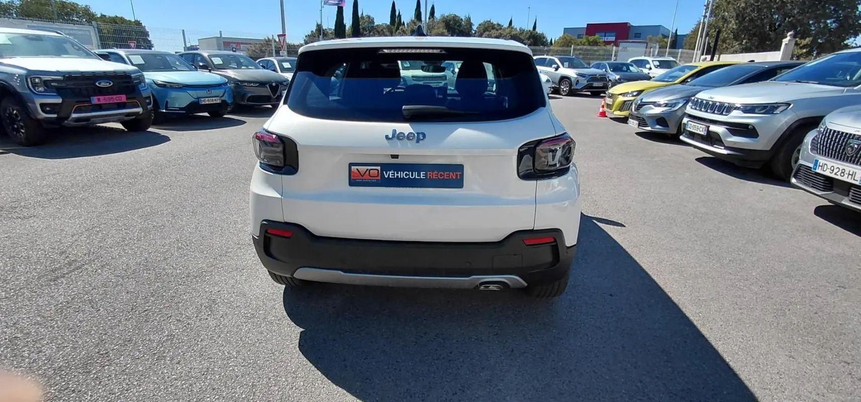 Vue arrière d'un Jeep Avenger blanc 2025 avec feux arrière noirs et pare-chocs noir dans un parking extérieur.