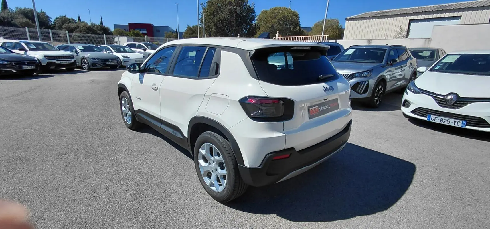 Jeep Avenger blanc vue 3/4 arrière droit, avec feux arrière sombres et jantes argentées, stationné en extérieur.
