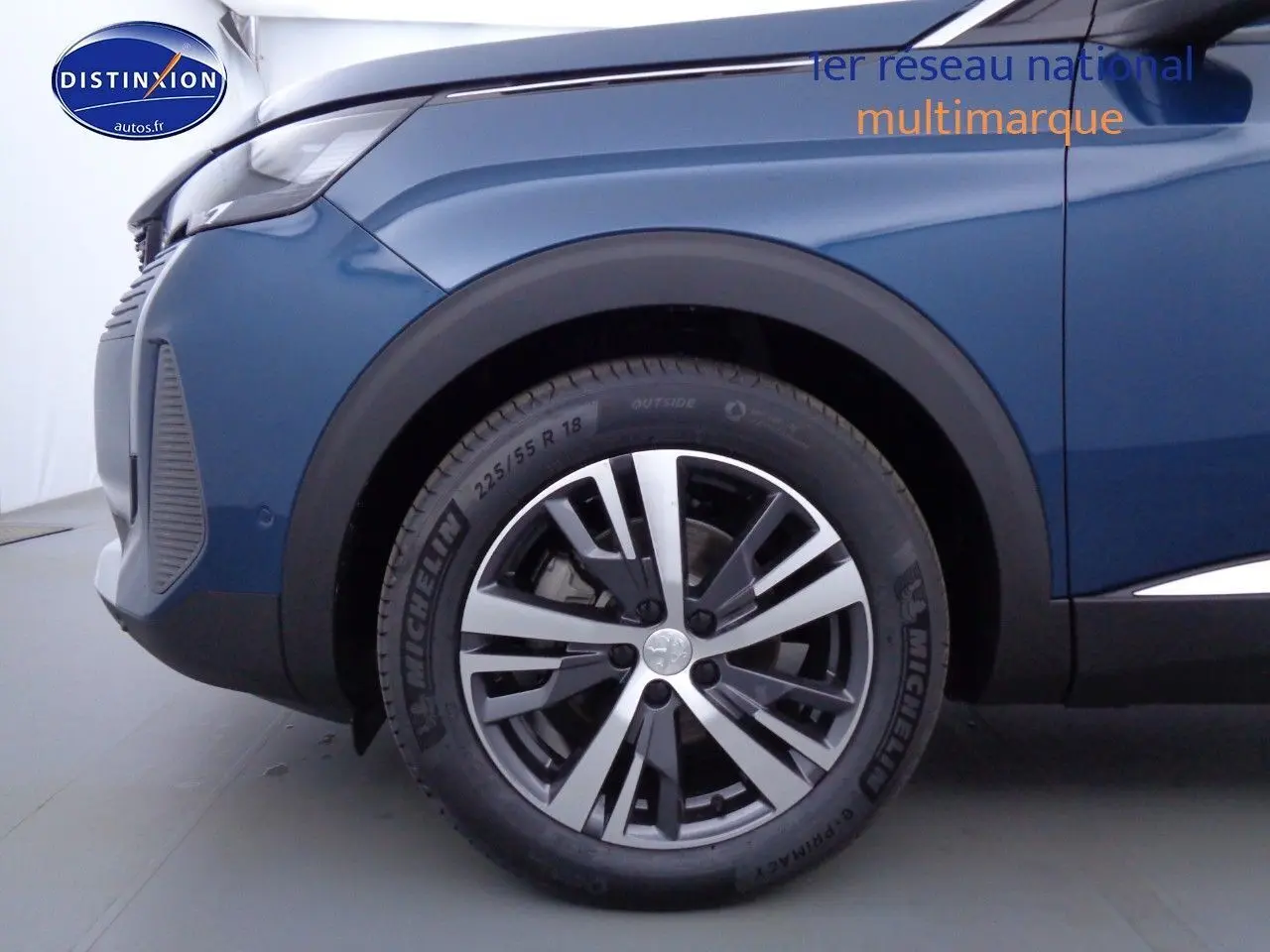 Gros plan sur la roue avant gauche d'un Peugeot 3008 2023 bleu Celebes métal avec jante alliage bicolore.