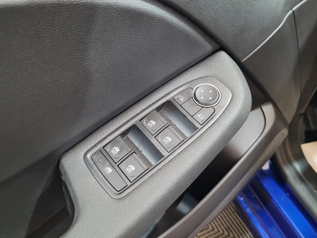 Gros plan sur la commande des vitres électriques côté conducteur d'une Renault Clio bleu 2025, intérieur noir.