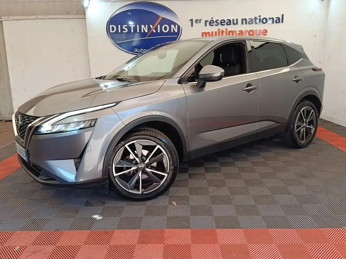Nissan Qashqai gris foncé en 3/4 avant droit, avec jantes alliage et phares LED allumés, intérieur visible.
