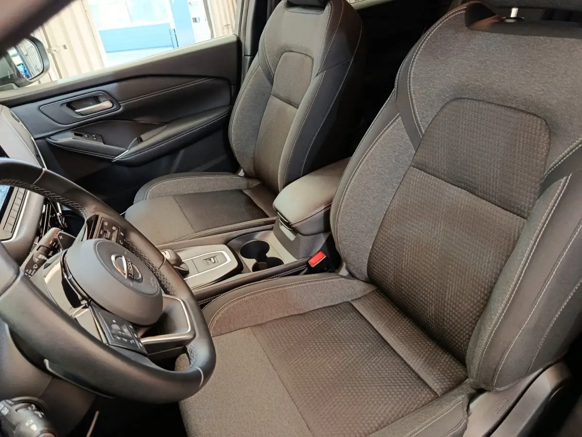 Vue intérieure côté conducteur du Nissan Qashqai 2022, sièges tissu gris et volant cuir multifonctions.