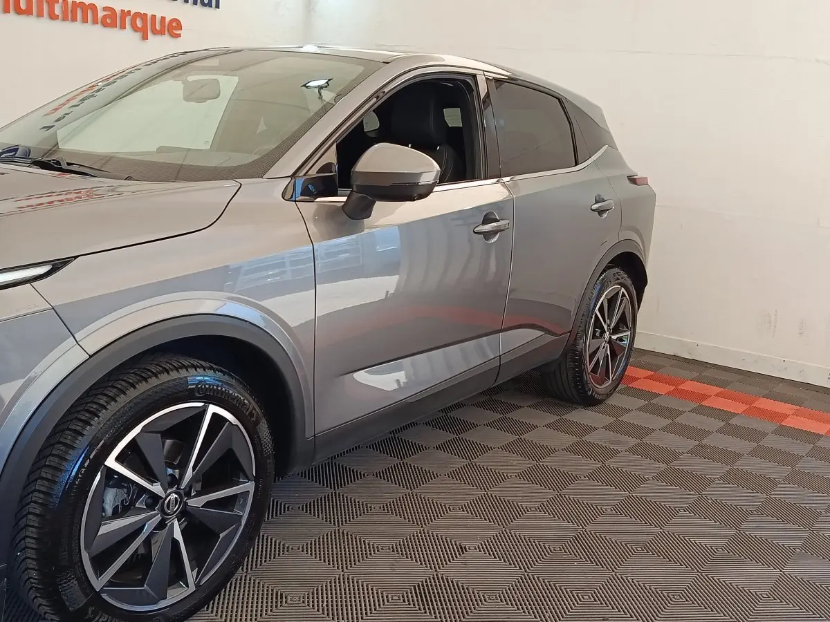 Vue 3/4 avant droit du Nissan Qashqai gris foncé avec jantes alliage noires et grises, intérieur visible côté conducteur.