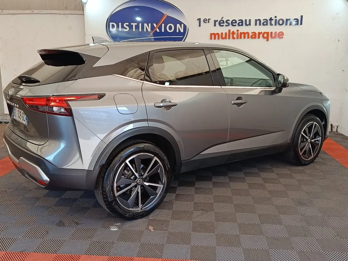 Vue 3/4 arrière droite d’un Nissan Qashqai gris foncé avec jantes alliage et feux arrière LED, en intérieur showroom.