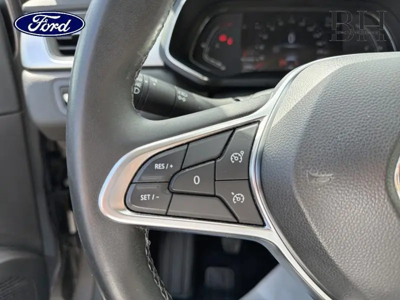 Gros plan sur les commandes du régulateur de vitesse à gauche du volant du Renault Captur gris Cassiopée, intérieur noir.