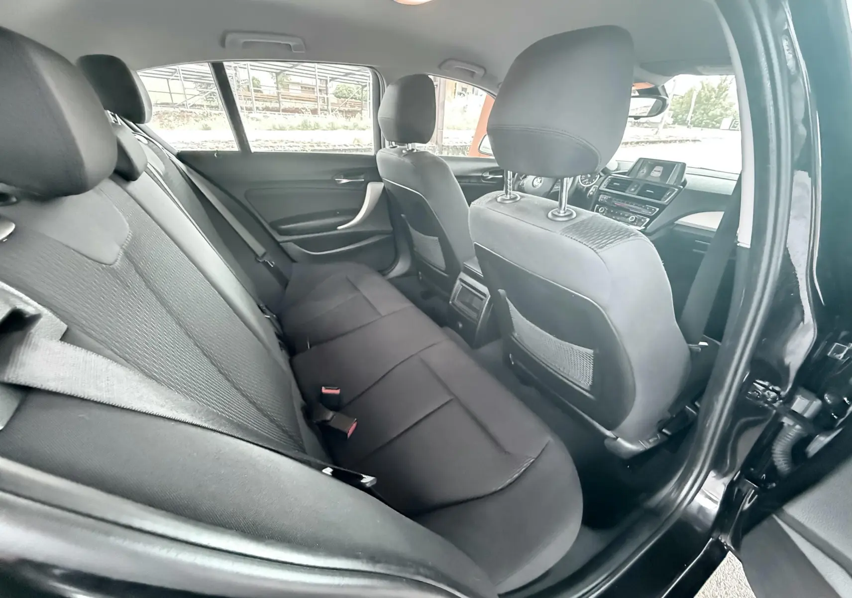 Vue intérieure arrière côté gauche d'une BMW Série 1 noire de 2016, montrant les sièges en tissu noir et l'avant du tableau de bord.