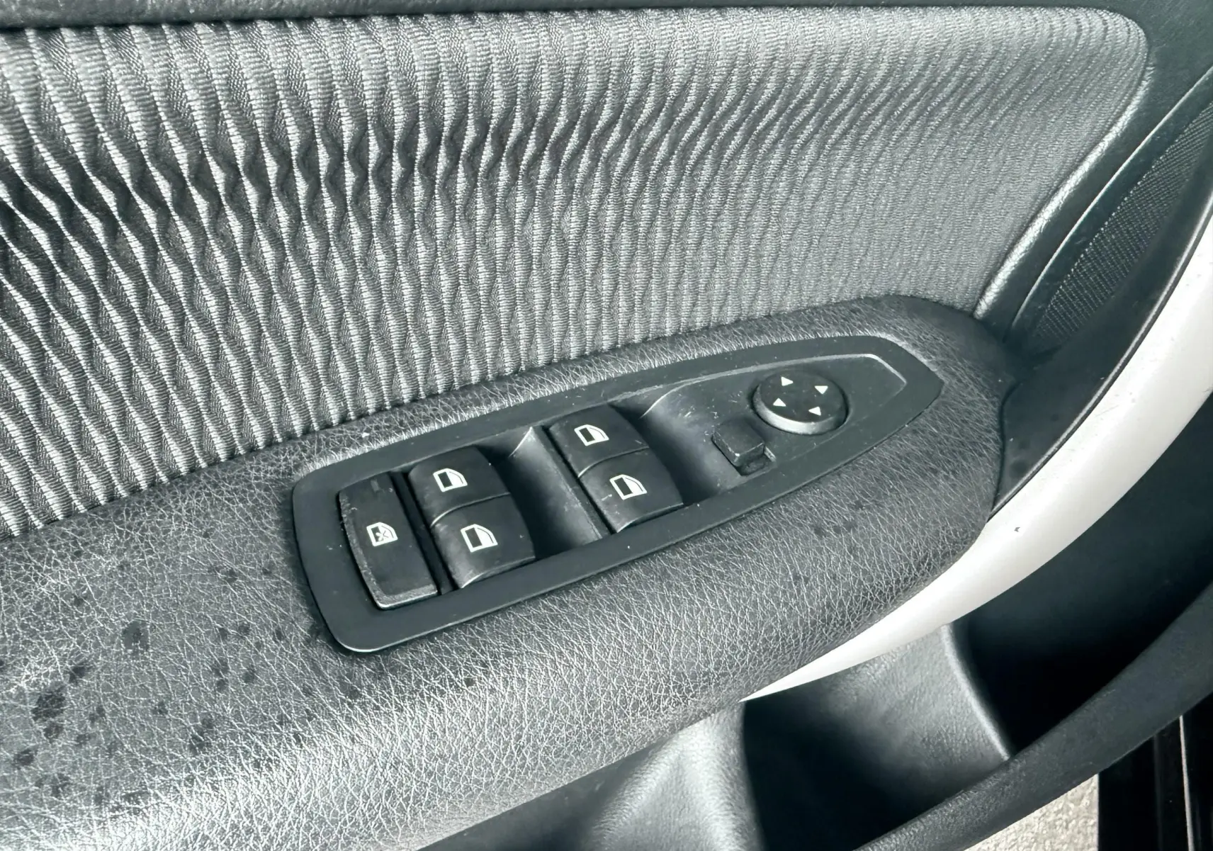 Gros plan sur les commandes de lève-vitres et réglage des rétroviseurs sur la porte côté conducteur d'une BMW Série 1 noire.