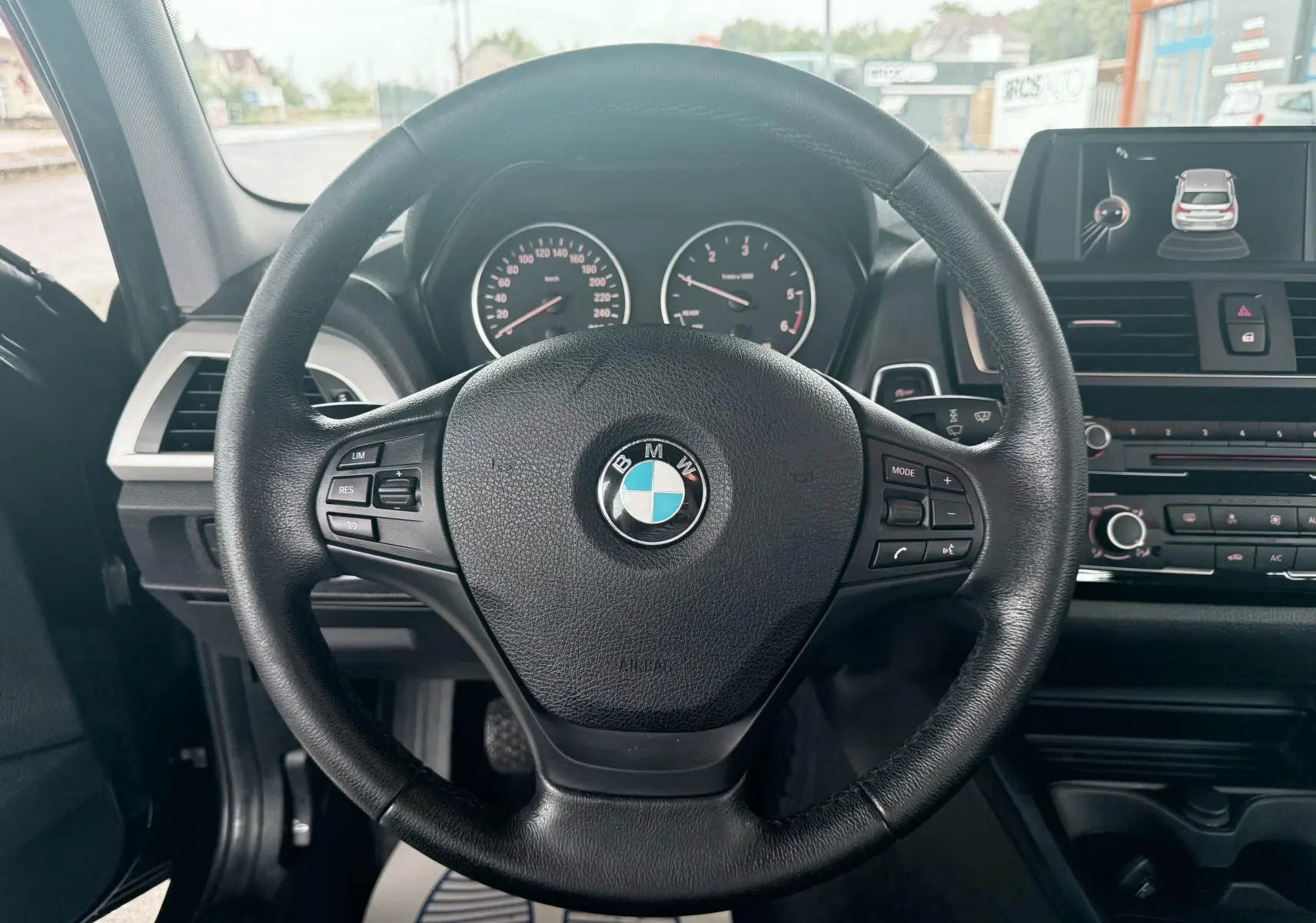 Vue intérieure centrée sur le volant noir de la BMW Série 1 avec tableau de bord et écran multimédia visibles.