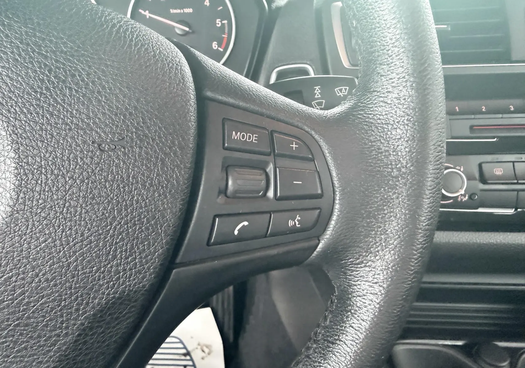 Gros plan sur le volant noir de la BMW Série 1 2016 avec commandes audio et téléphone intégrées.