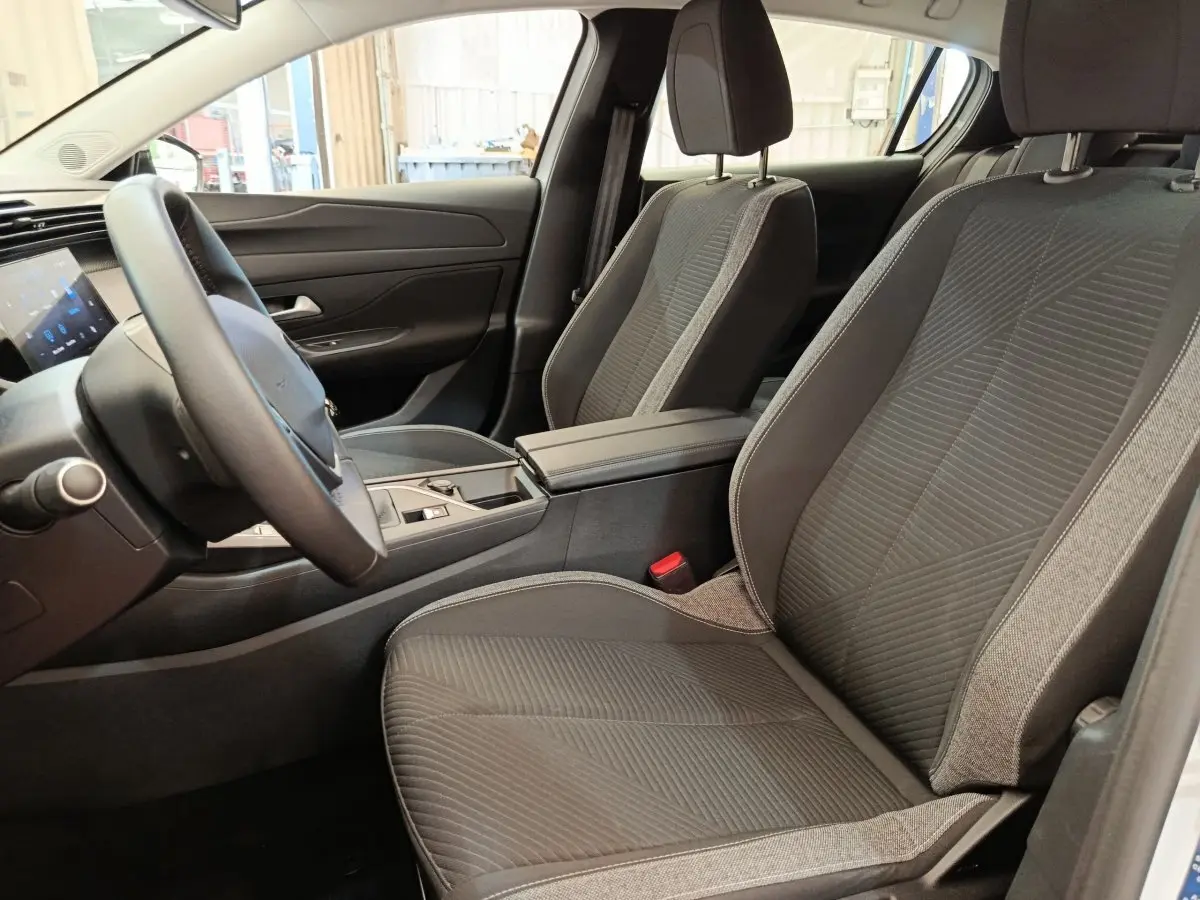Vue intérieure côté conducteur de la Peugeot 308 2024 avec sièges tissu gris et volant cuir multifonctions.