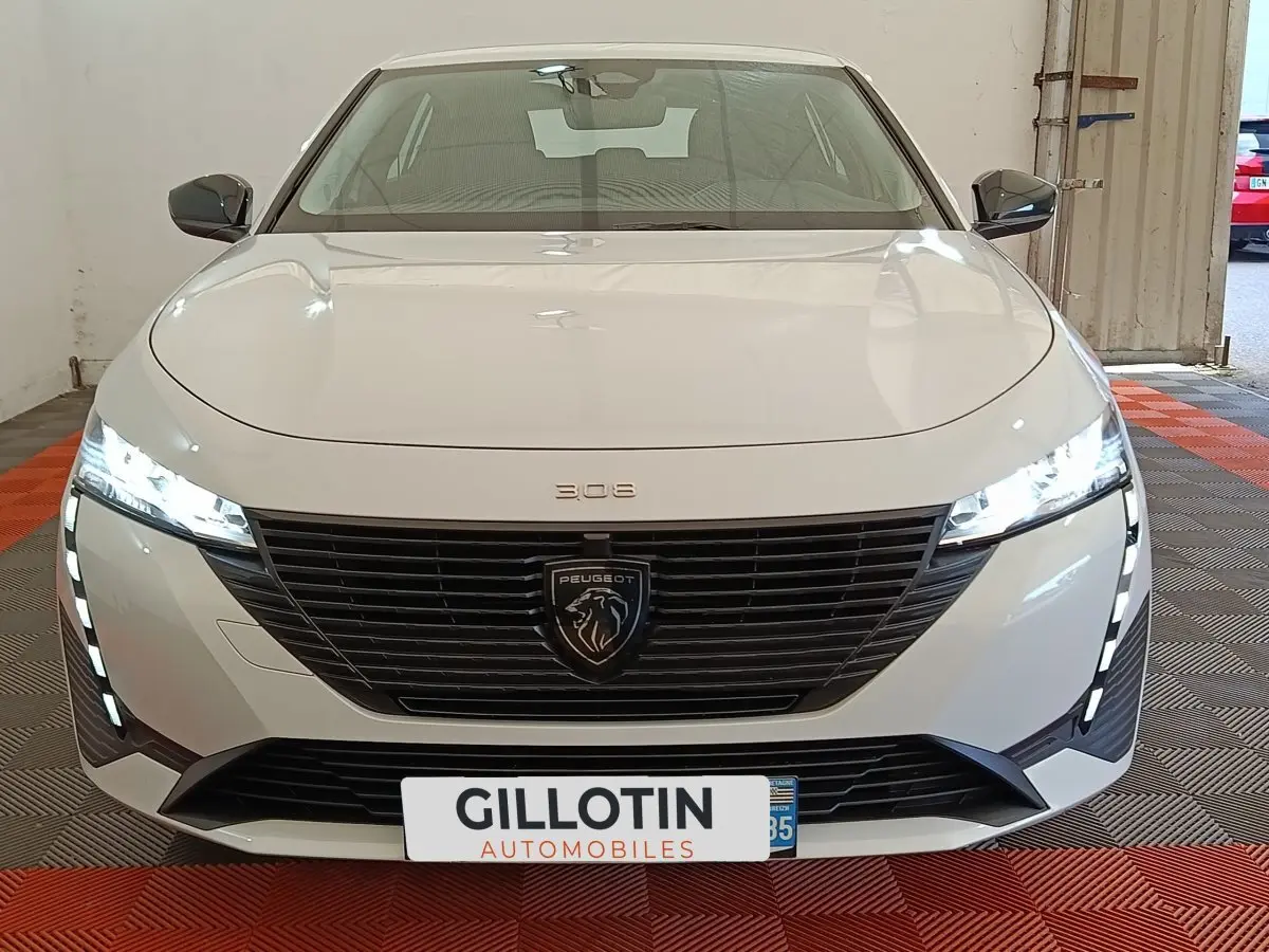 Vue frontale d'une Peugeot 308 blanche 2024 avec calandre noire et feux LED allumés en intérieur.