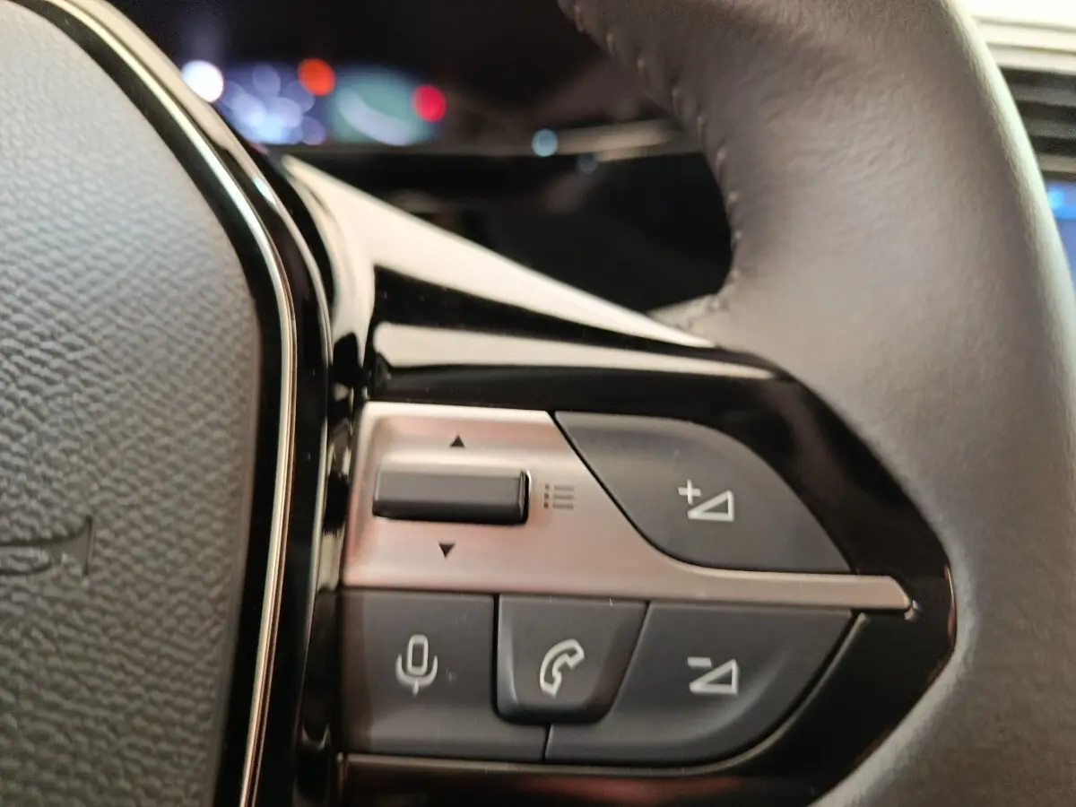 Gros plan sur les commandes multifonctions côté gauche du volant cuir d'une Peugeot 308 blanche 2024.