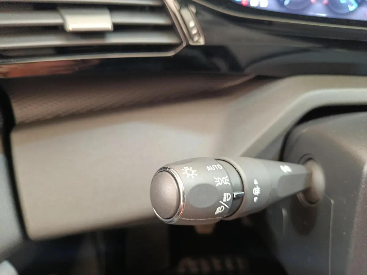Gros plan sur la commande des phares à gauche du volant dans l'habitacle d'une Peugeot 308 blanche 2024.