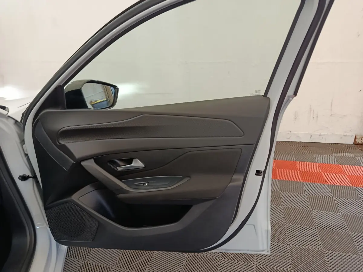 Vue intérieure de la porte avant gauche d'une Peugeot 308 blanche, mettant en valeur les commandes et le revêtement noir.