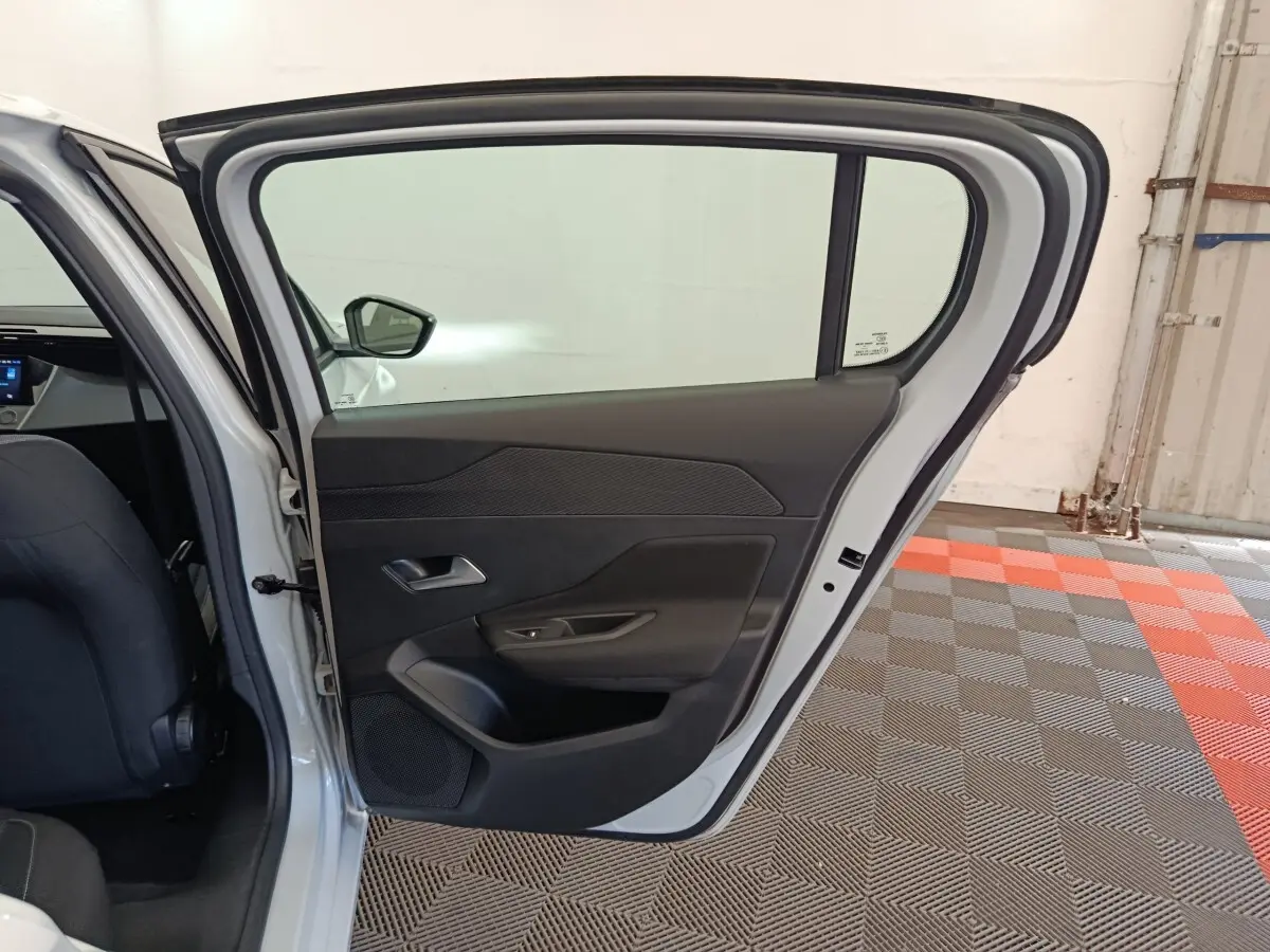 Vue intérieure de la porte arrière gauche ouverte d'une Peugeot 308 blanche, avec garniture noire et poignée intégrée.