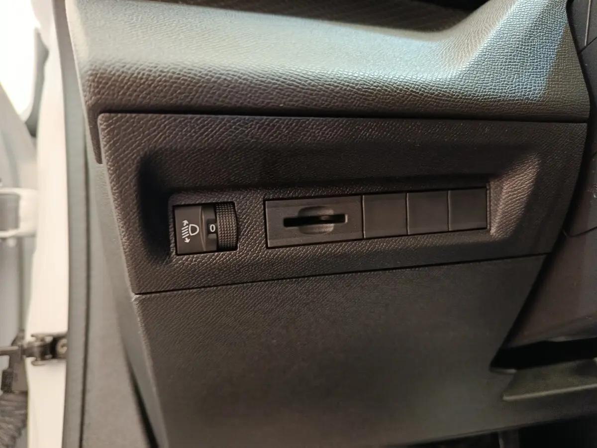 Détail intérieur côté gauche avec commandes de réglage des phares sur Peugeot 308 blanc 2024 Active Pack.