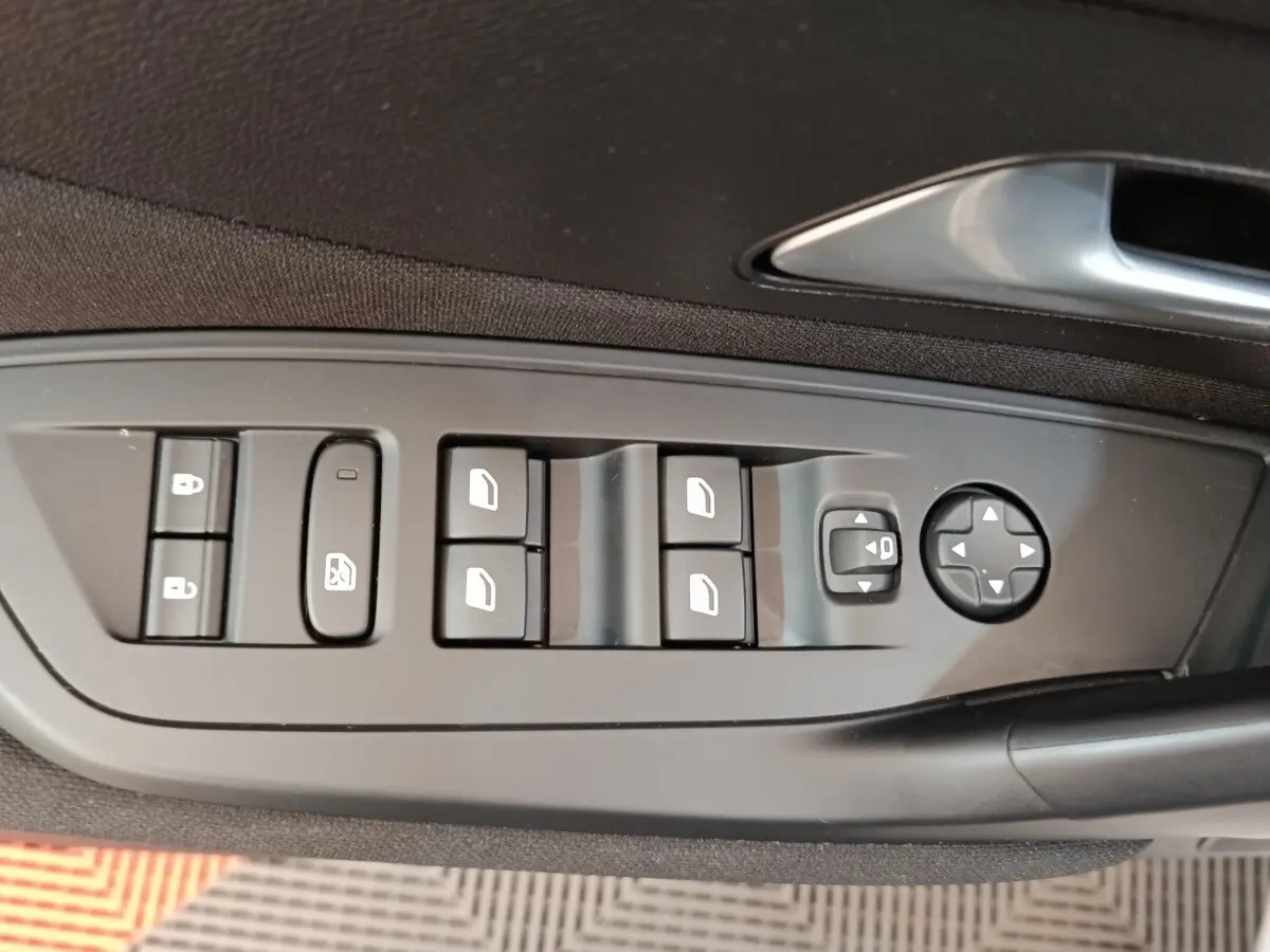 Gros plan sur les commandes de lève-vitres et rétroviseurs côté conducteur d'une Peugeot 308 blanche 2024.
