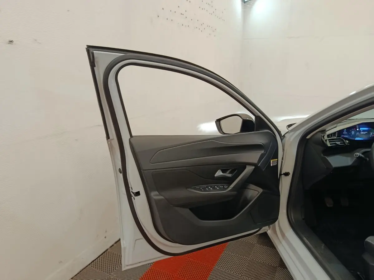 Portière avant gauche ouverte d’une Peugeot 308 blanche, montrant l’intérieur noir et les commandes de vitres.