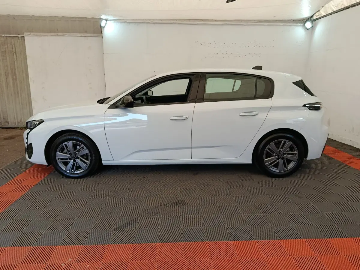 Peugeot 308 blanche vue de profil côté gauche, avec jantes alliage et poignées de porte ton carrosserie.