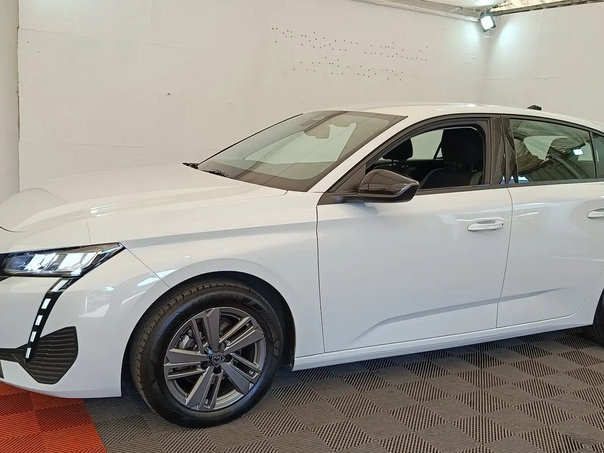 Profil droit de la Peugeot 308 blanche 2024 ACTIVE PACK avec jantes alliage et feux LED distinctifs allumés.