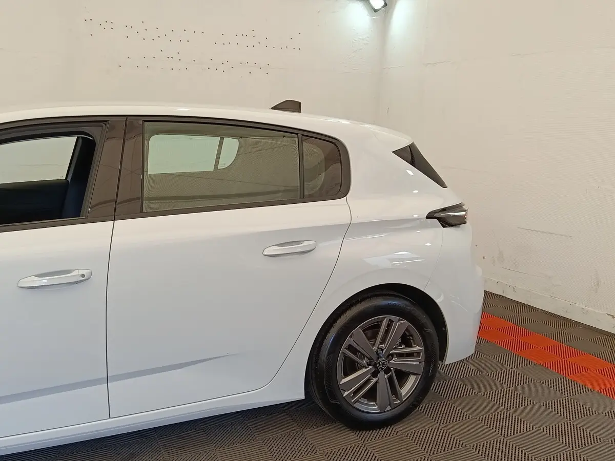 Vue latérale côté droit d'une Peugeot 308 blanche 2024, mettant en valeur la porte arrière et la roue arrière alliage.