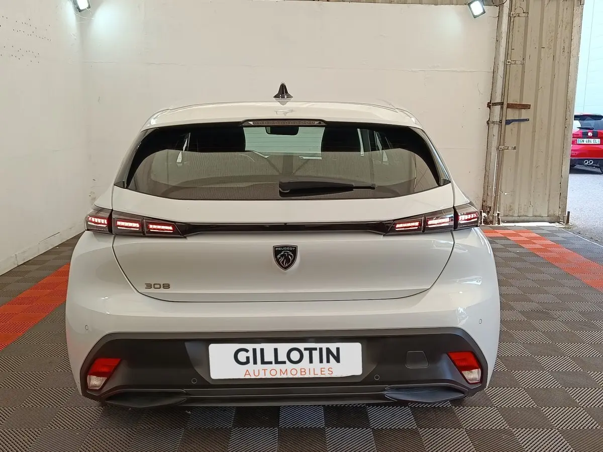 Vue arrière d'une Peugeot 308 blanche 2024 avec feux LED allumés dans un garage.