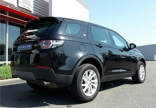 Vue 3/4 arrière droite d'un Land Rover Discovery Sport Mark II noir, avec jantes argentées, stationné devant un bâtiment moderne.