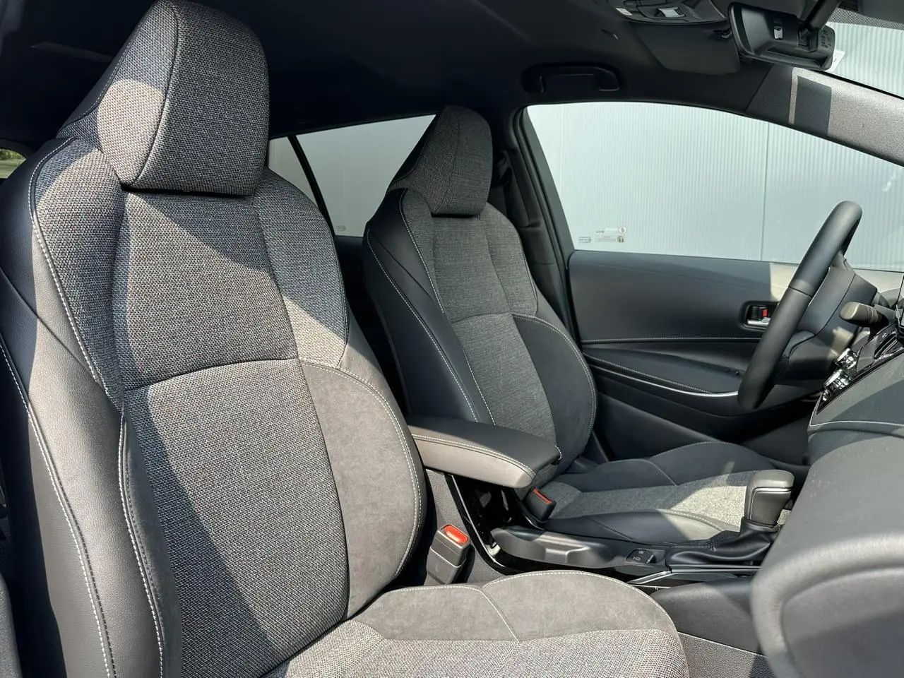 Intérieur avant de la Toyota Corolla Touring Sport 2025, sièges tissu gris et alcantara avec accoudoir central noir.