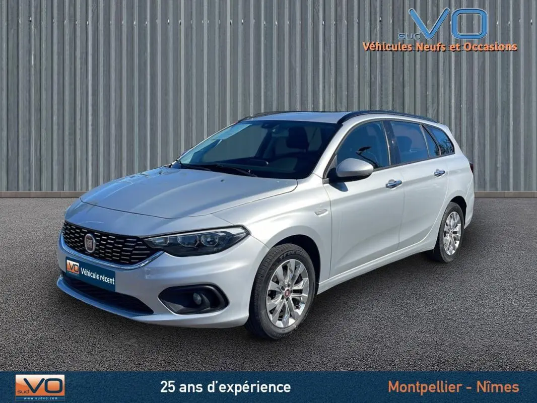 Fiat Tipo Station Wagon gris en 3/4 avant droit, avec jantes alliage et barres de toit visibles.