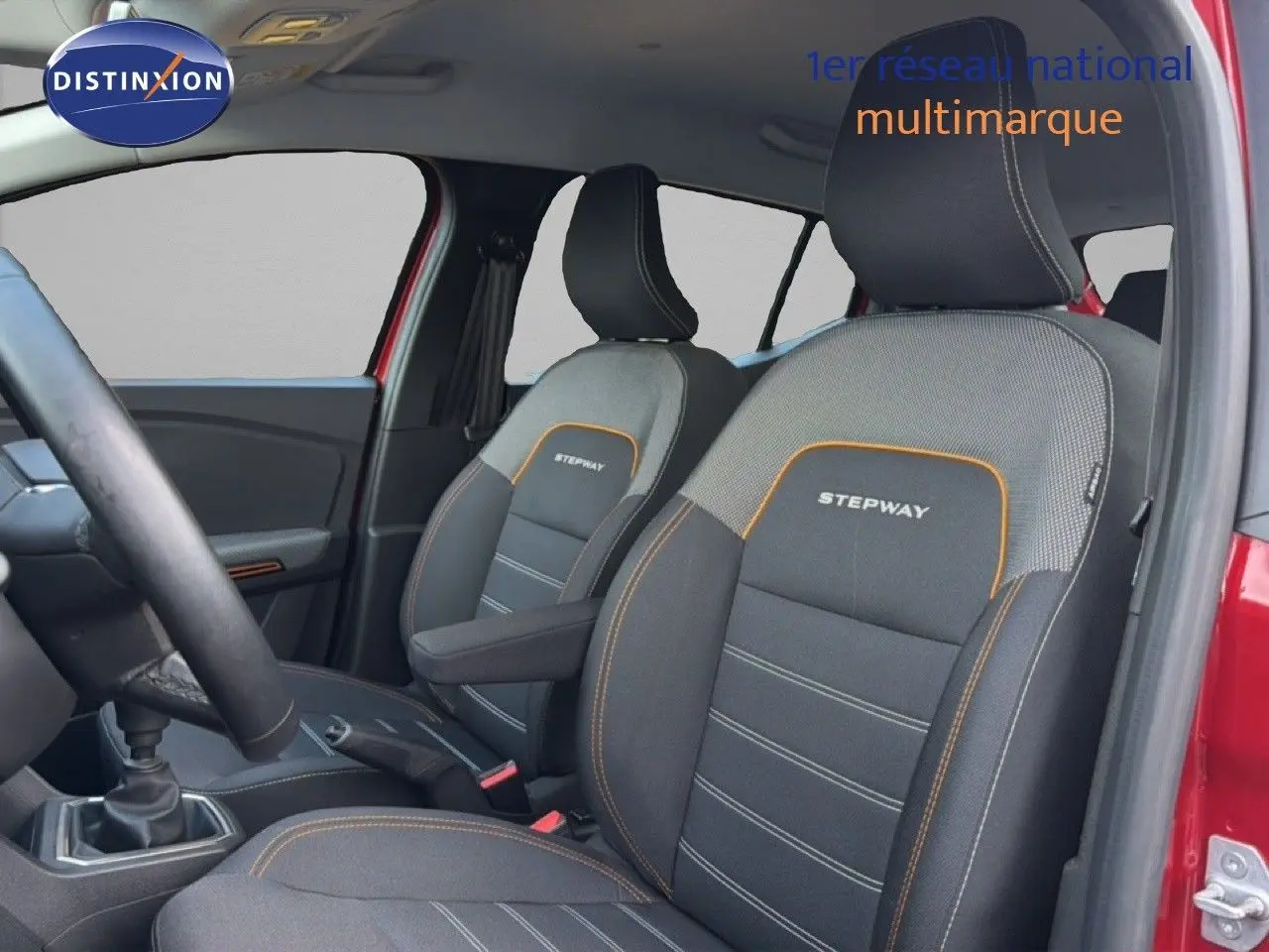 Vue intérieure côté conducteur de la Dacia Sandero Stepway rouge fusion, mettant en valeur les sièges noirs avec surpiqûres orange et logo Stepway.