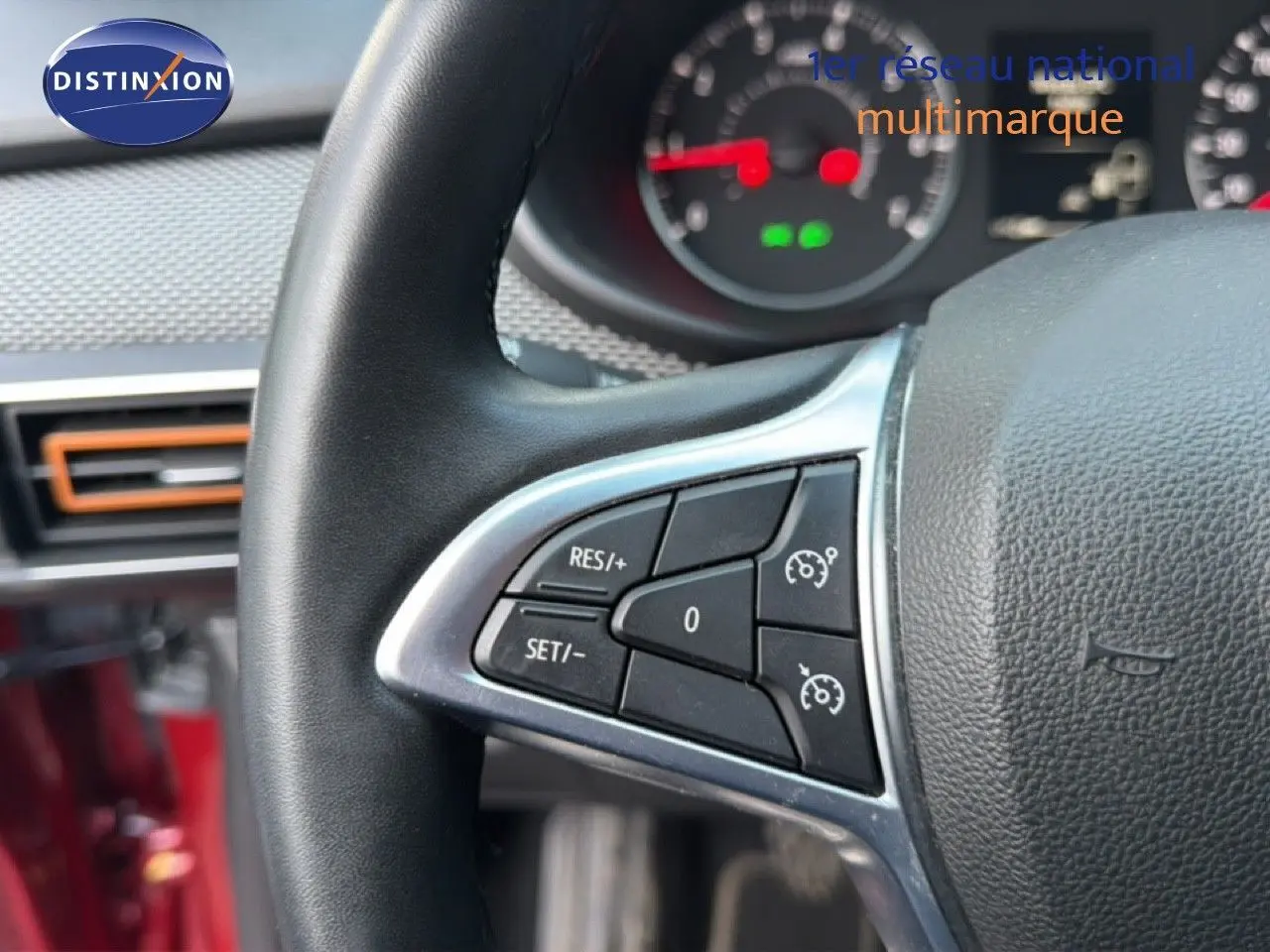 Gros plan sur le volant avec commandes de régulateur de vitesse, intérieur rouge fusion visible en arrière-plan.