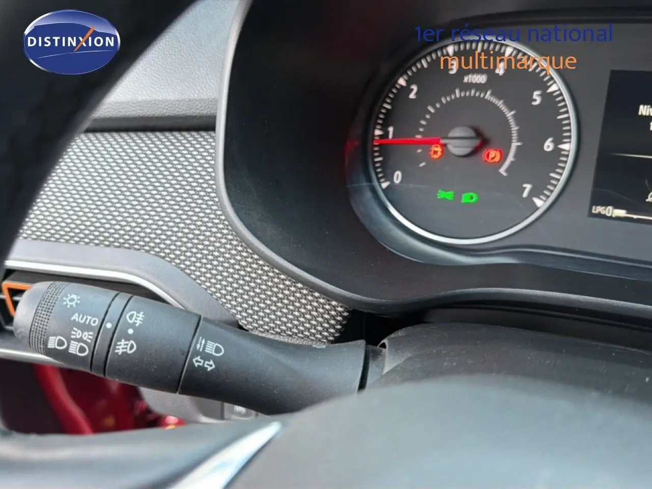 Gros plan sur le tableau de bord et le commodo gauche d’une Dacia Sandero Stepway rouge fusion, affichant le compte-tours et témoins lumineux.