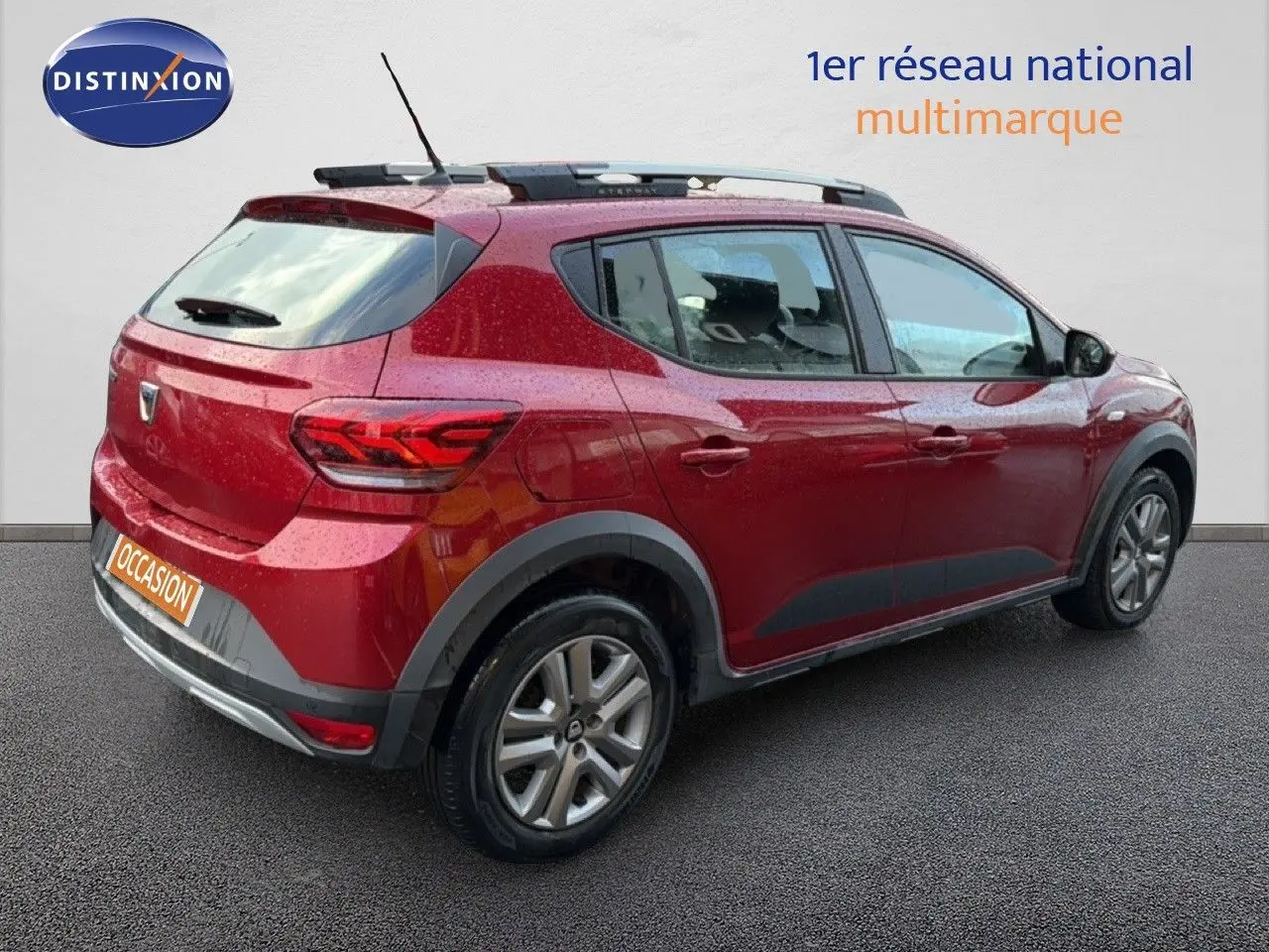 Vue 3/4 arrière droite d'une Dacia Sandero Stepway rouge fusion avec barres de toit et jantes alliage.