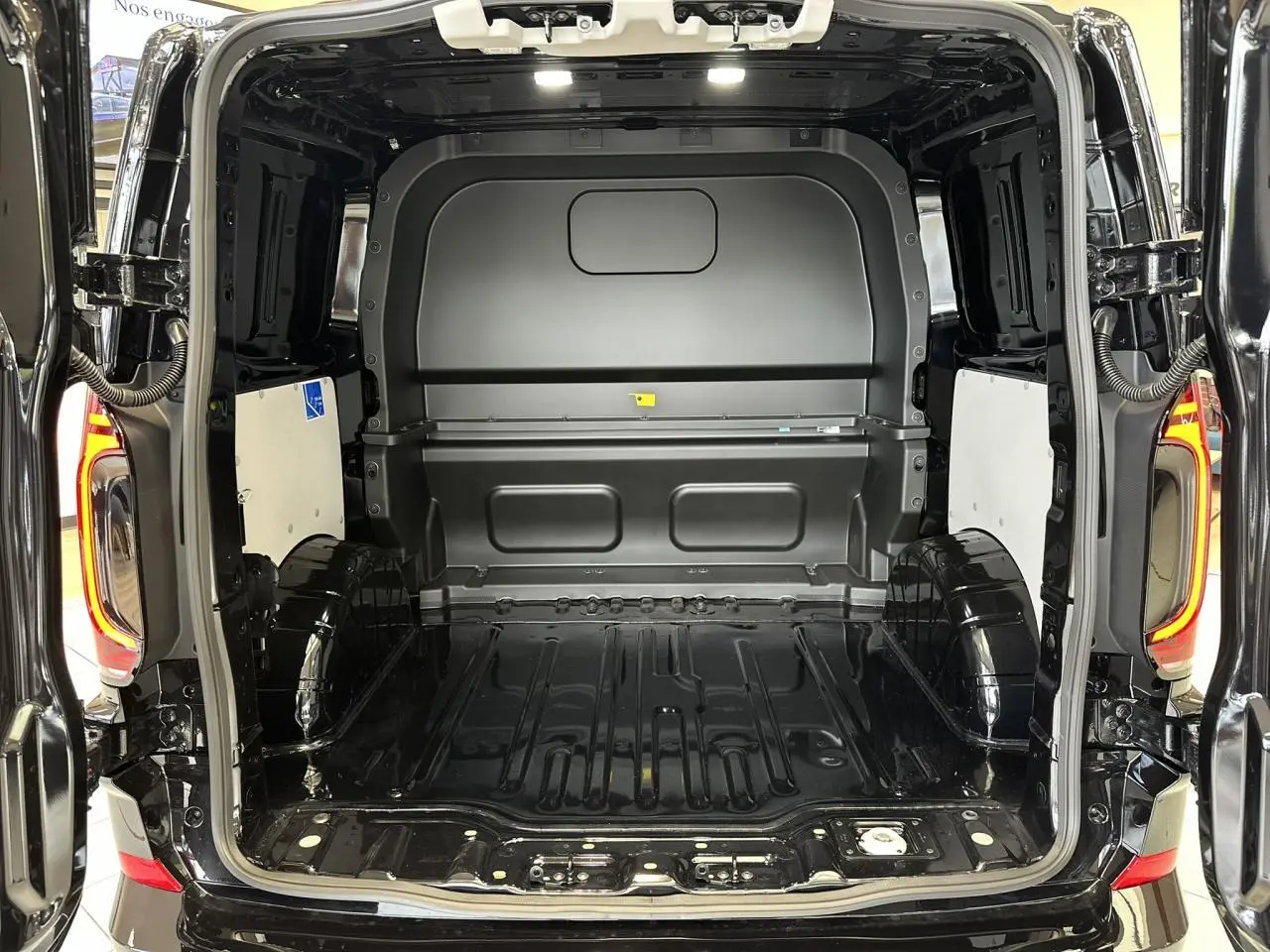 Vue arrière ouverte du Volkswagen Transporter T7 ProCab noir Minuit, montrant l'espace de chargement vide et les feux arrière LED allumés.