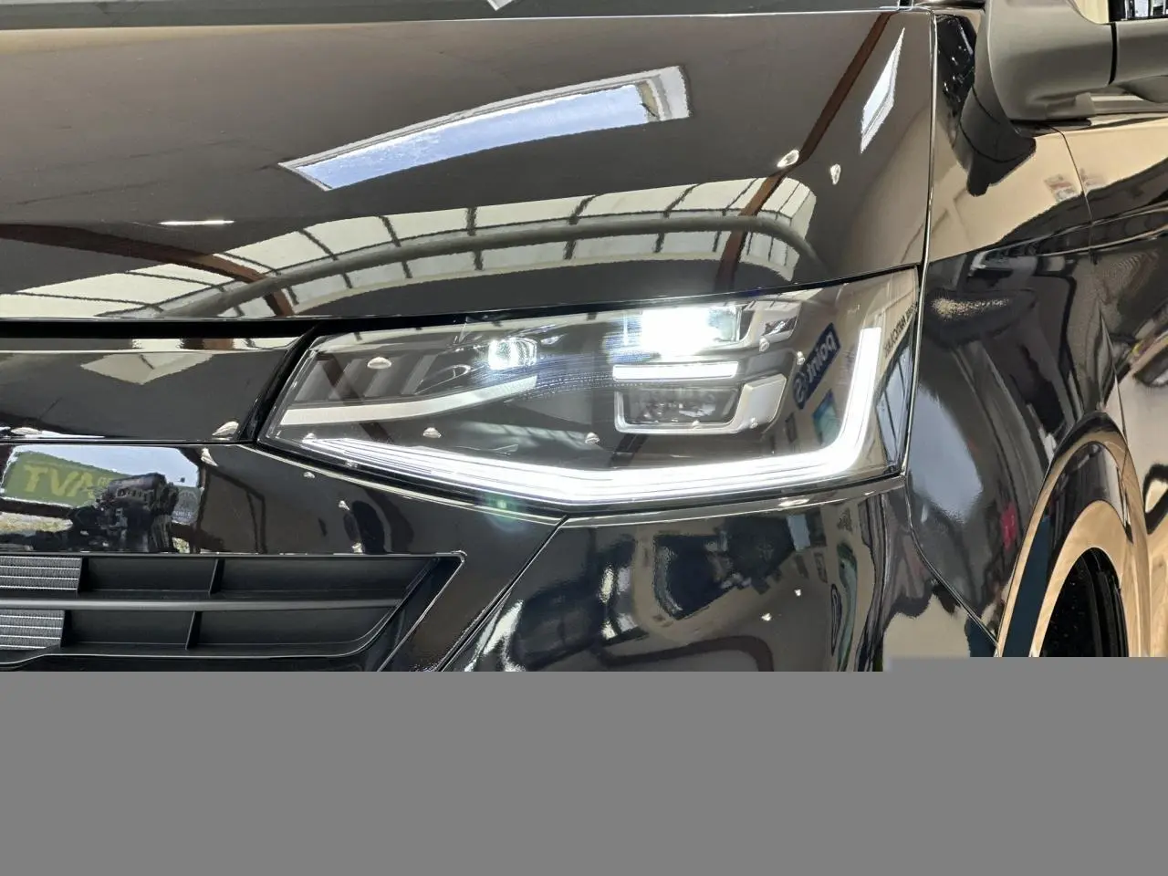 Gros plan sur le phare avant droit LED allumé du Volkswagen Transporter T7 ProCab noir Minuit, avec calandre partielle visible.