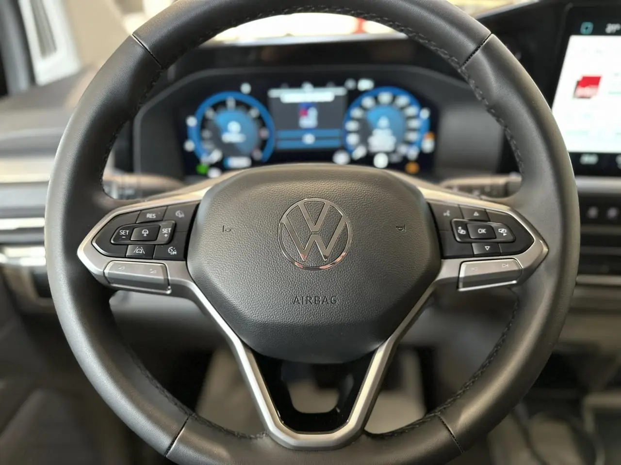 Vue rapprochée du volant multifonction en similicuir noir du Volkswagen Transporter T7 avec tableau de bord numérique en arrière-plan.