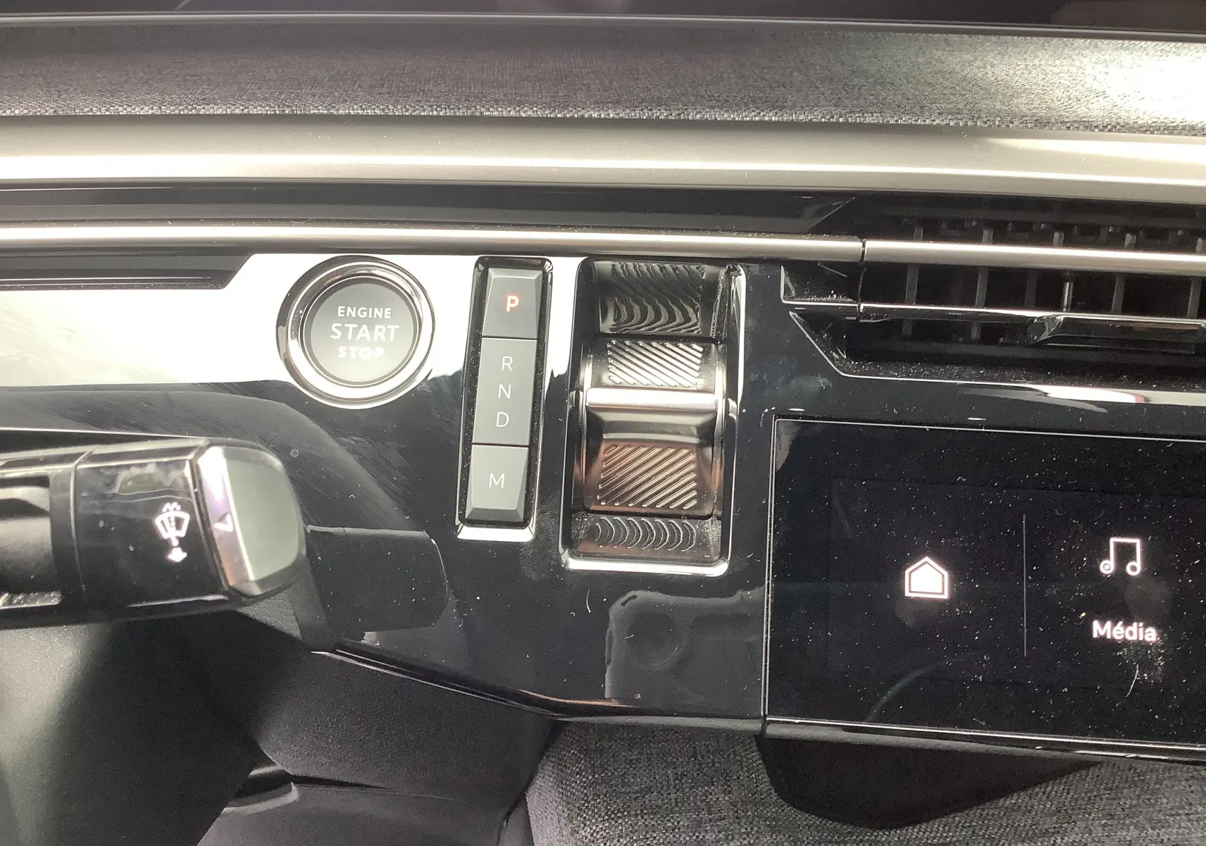 Gros plan sur la console centrale noire brillante du Peugeot 3008 Hybrid 2024, avec bouton start/stop et sélecteur de vitesse tactile.