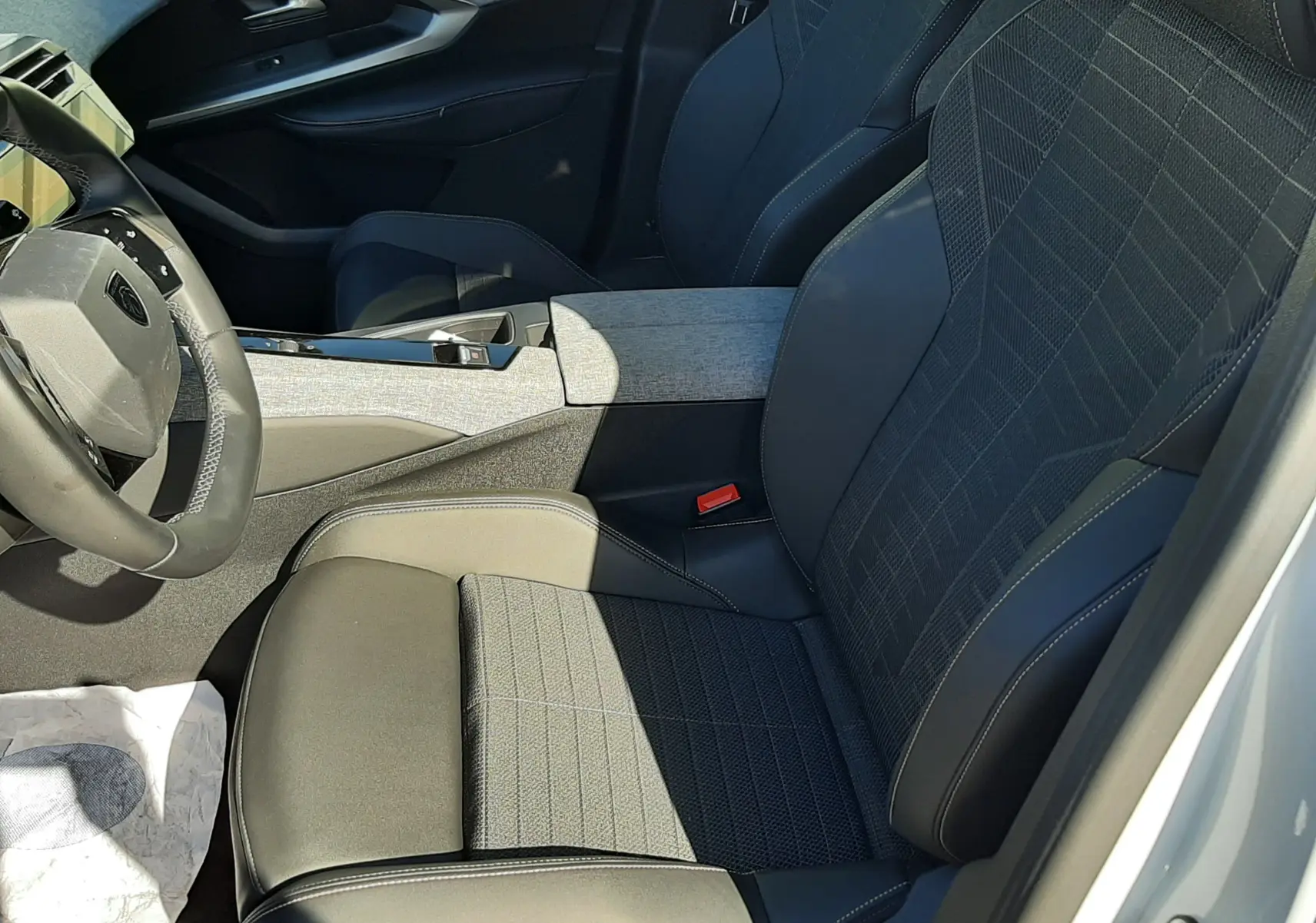 Vue intérieure côté conducteur du Peugeot 3008 Hybrid 2024 avec sièges noirs en tissu et cuir, et accoudoir central gris.