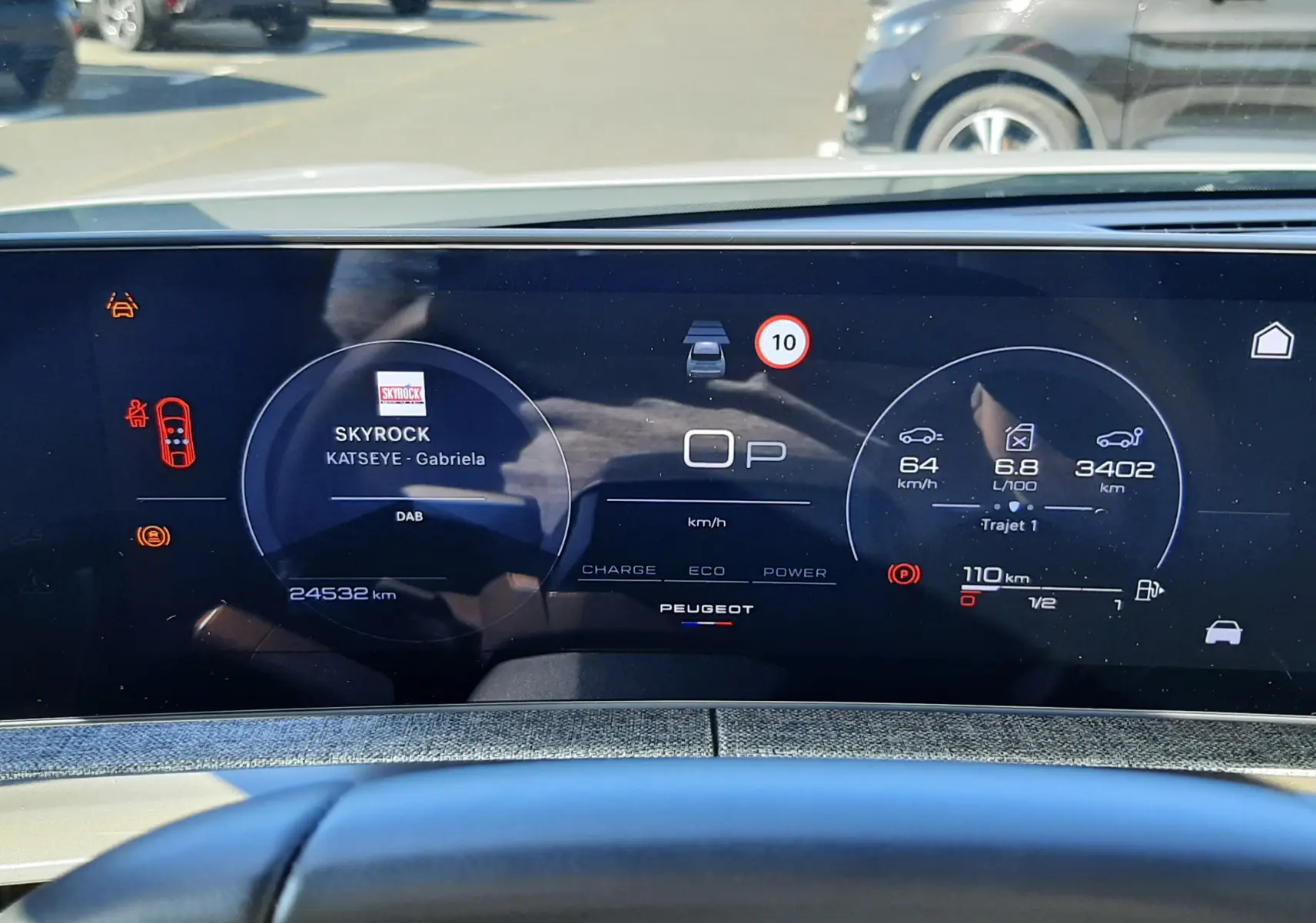 Tableau de bord numérique du Peugeot 3008 Hybrid blanc, affichant vitesse, consommation et station radio Skyrock.