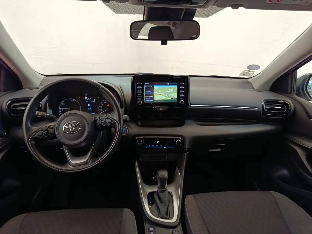 Vue intérieure frontale du tableau de bord et volant cuir noir de la Toyota Yaris hybride 2022 avec écran tactile central.