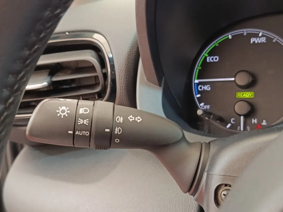 Gros plan sur la manette des phares et clignotants à gauche du volant dans l’habitacle gris clair de la Toyota Yaris hybride 2022.