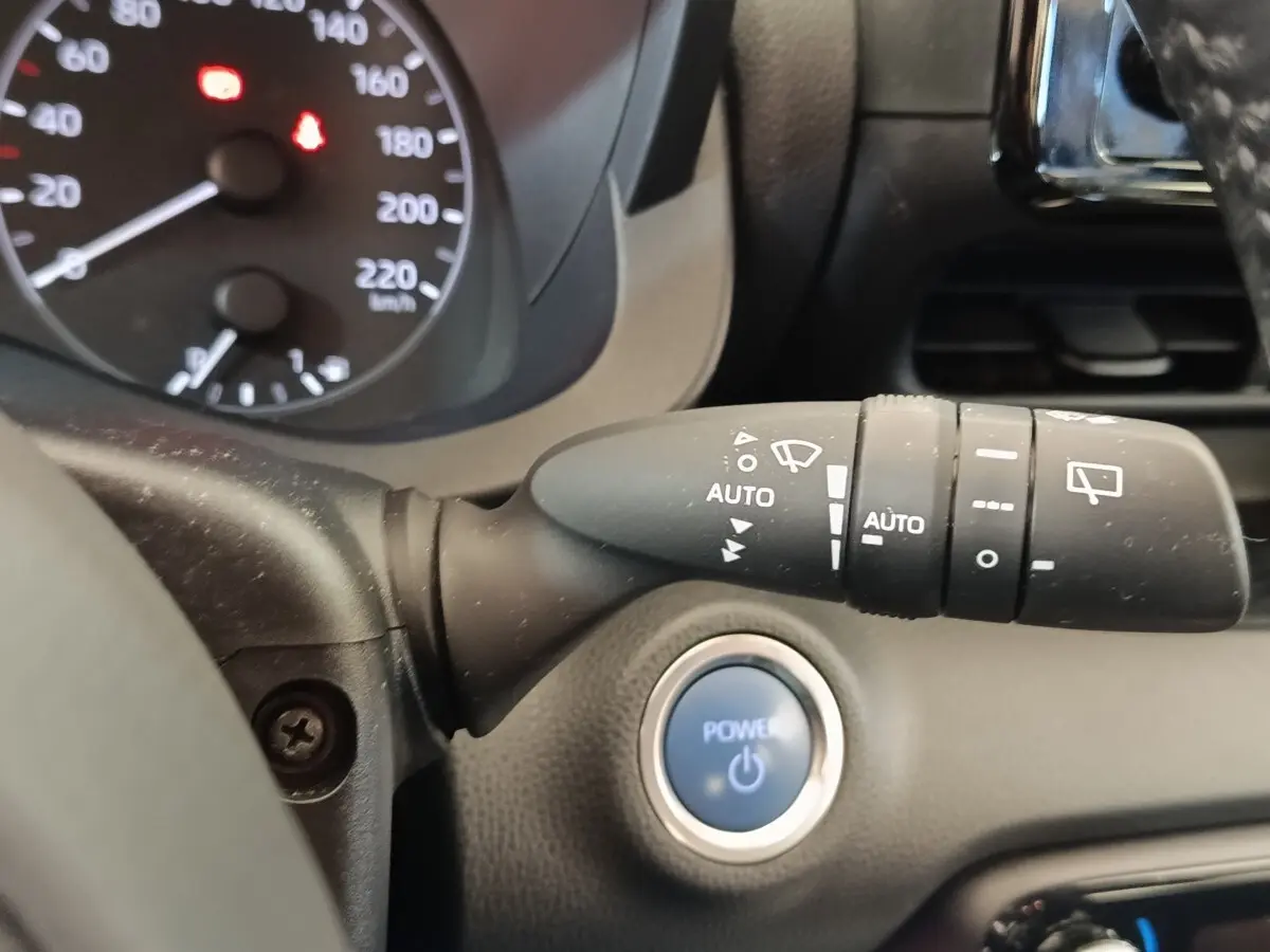 Gros plan sur la commande d’essuie-glace et le bouton start/stop bleu dans l’habitacle d’une Toyota Yaris gris clair.