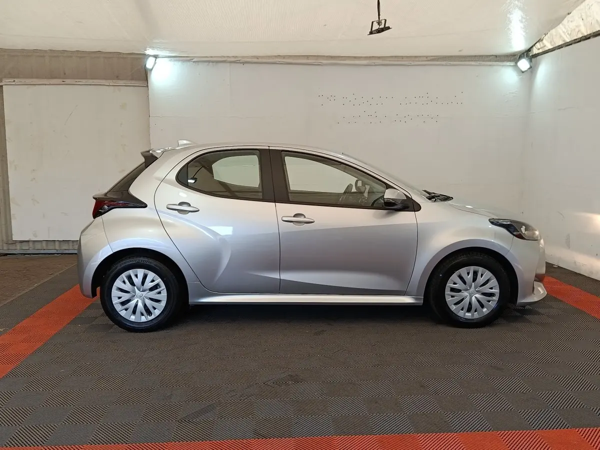 Profil droit d'une Toyota Yaris hybride gris clair 2022, avec jantes standard et lignes dynamiques visibles.