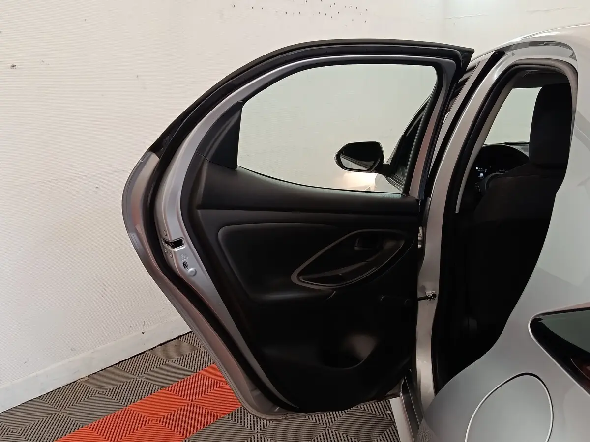 Vue arrière côté gauche de la Toyota Yaris hybride gris clair avec porte arrière ouverte et intérieur noir visible.