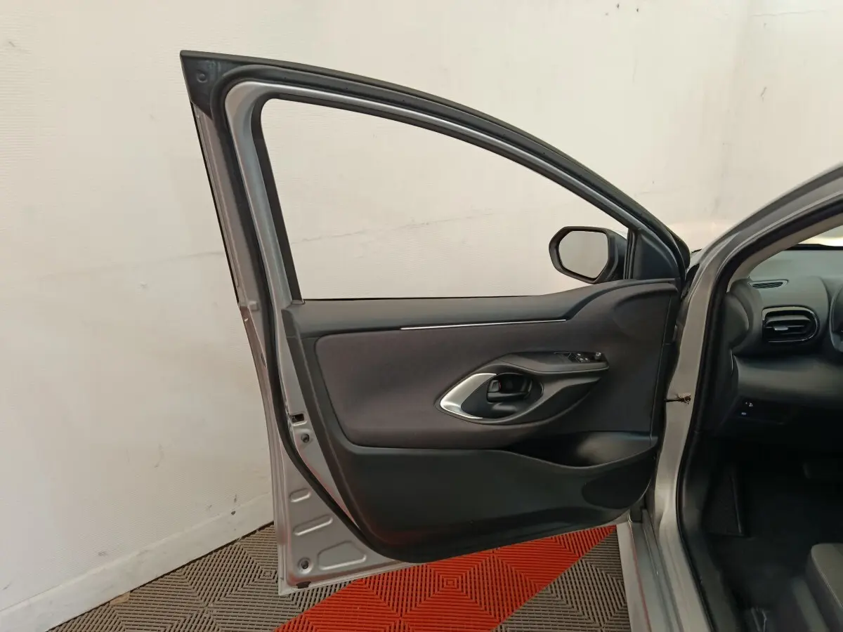 Porte avant gauche ouverte d'une Toyota Yaris hybride gris clair, montrant la garniture intérieure noire et poignée argentée.