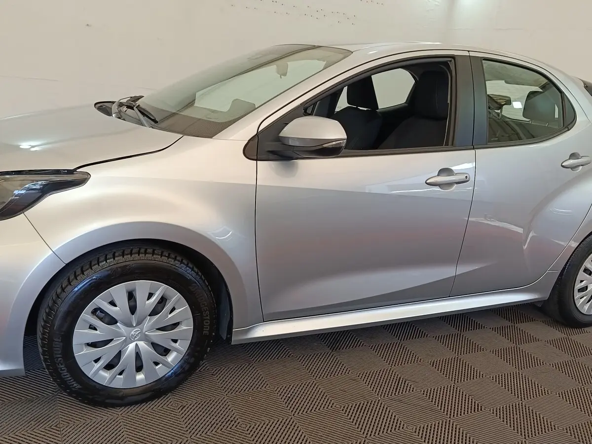 Profil côté gauche d'une Toyota Yaris hybride gris clair 2022, avec jantes et rétroviseur assortis.