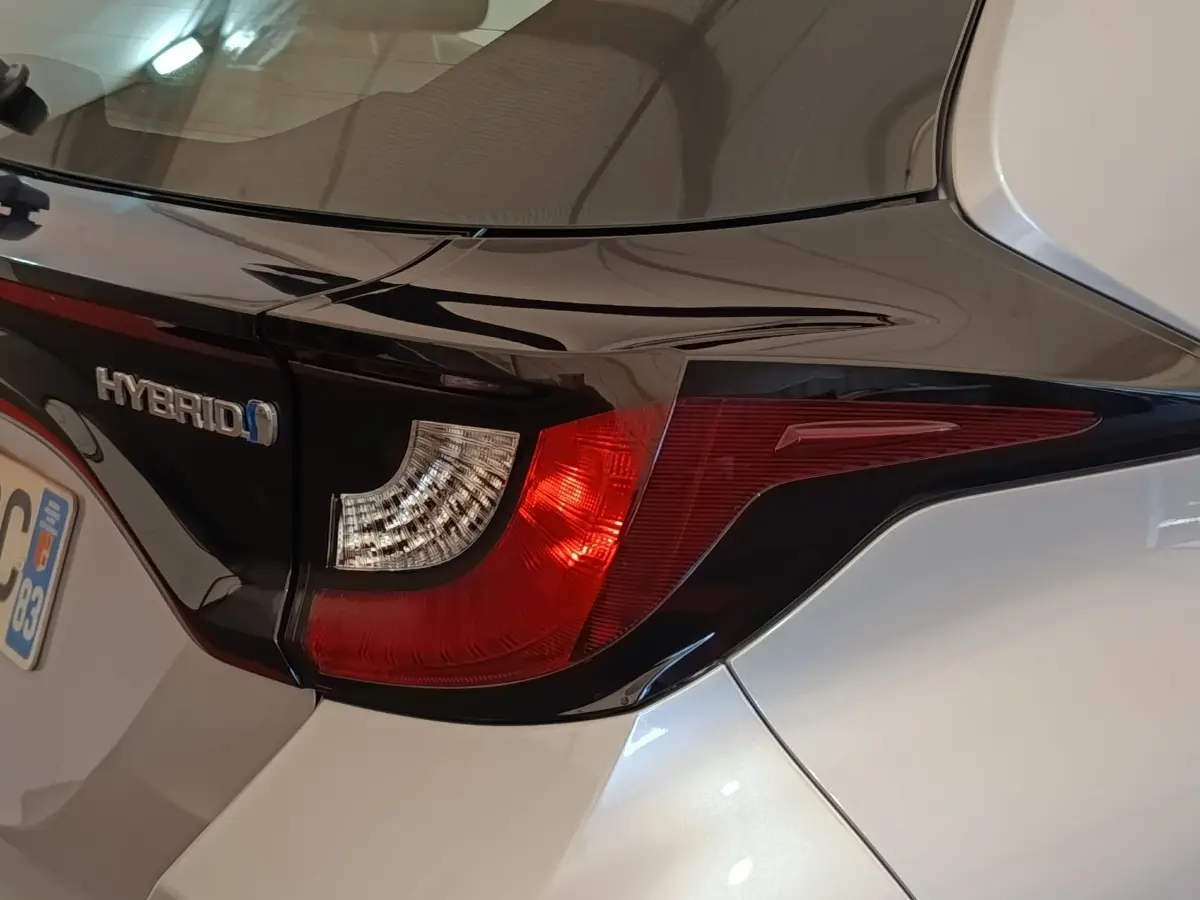 Gros plan sur le feu arrière droit gris clair d'une Toyota Yaris hybride avec logo Hybrid visible sur le coffre.