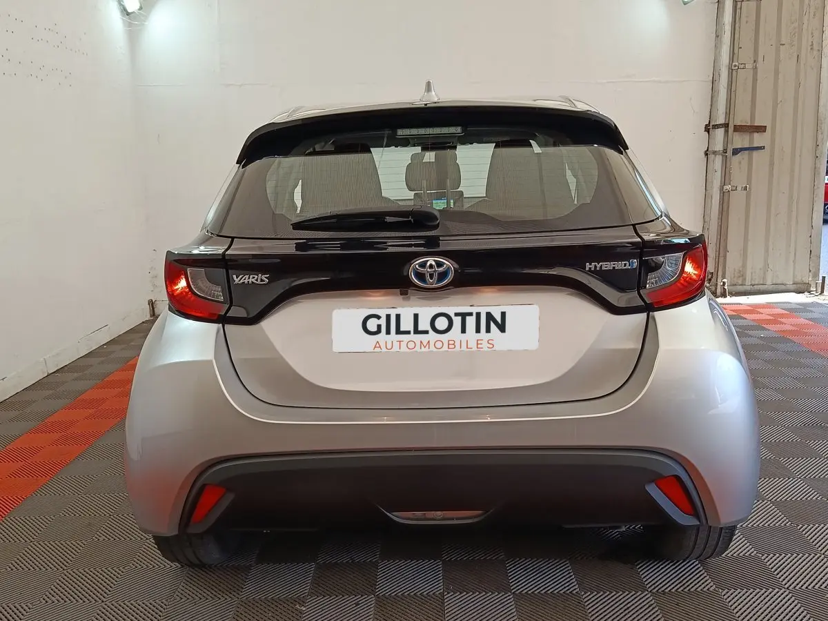 Vue arrière d'une Toyota Yaris hybride gris clair avec toit noir et feux arrière allumés dans un garage.