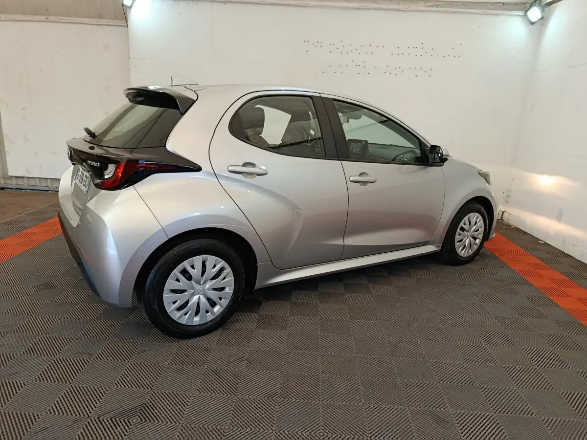Toyota Yaris hybride gris clair vue 3/4 arrière droit, avec toit noir et jantes standard en plastique.